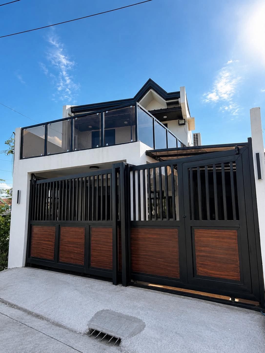A finished two-storey LSEE home with a black steel and hardwood gate, glass balcony railing and a roof deck