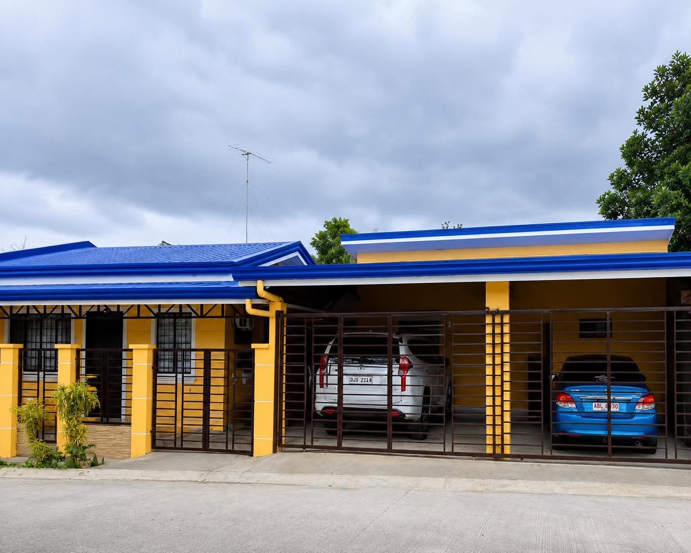 A finished bungalow with a blue metal roof, yellow walls and a covered two-car carport