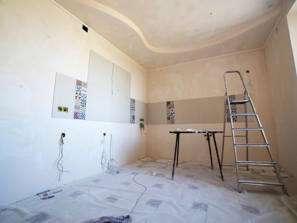 Room mid-renovation with fresh plaster, part-laid tiling and a stepladder