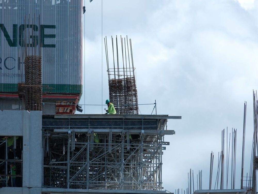 Rebar columns and shoring rising from a concrete frame under a heavy overcast sky