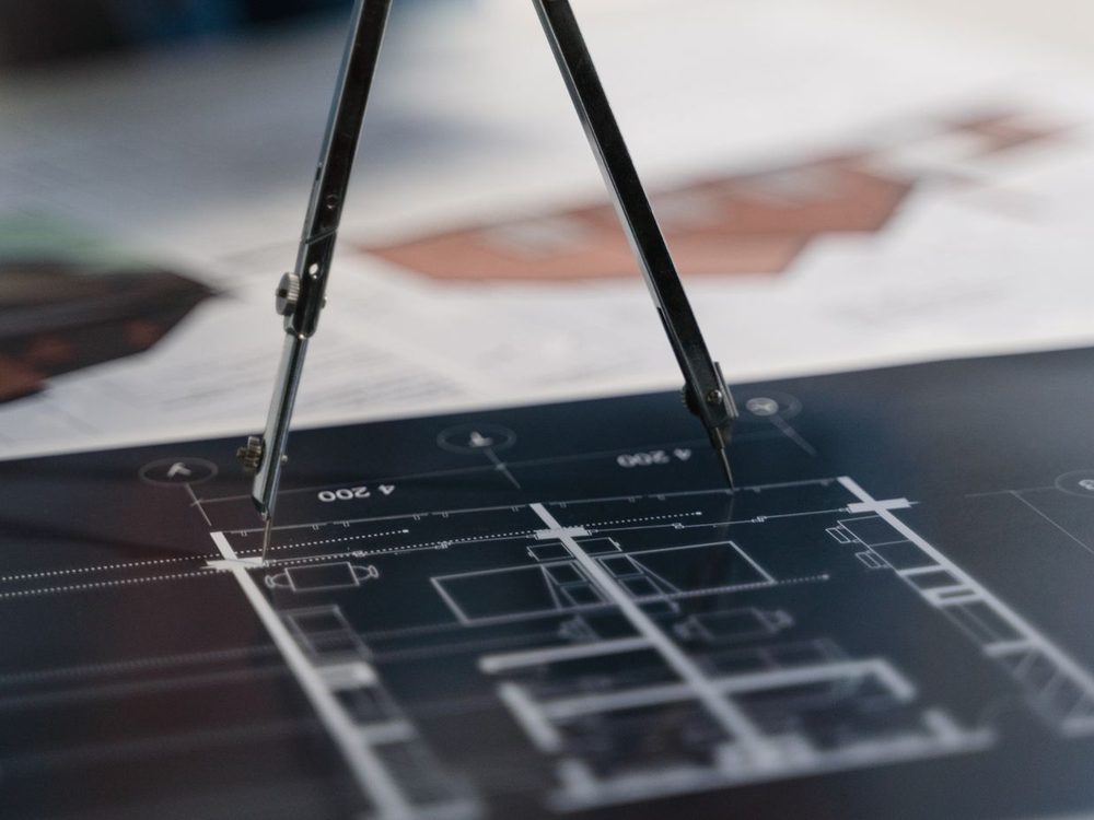 A drawing compass resting on a dimensioned technical drawing