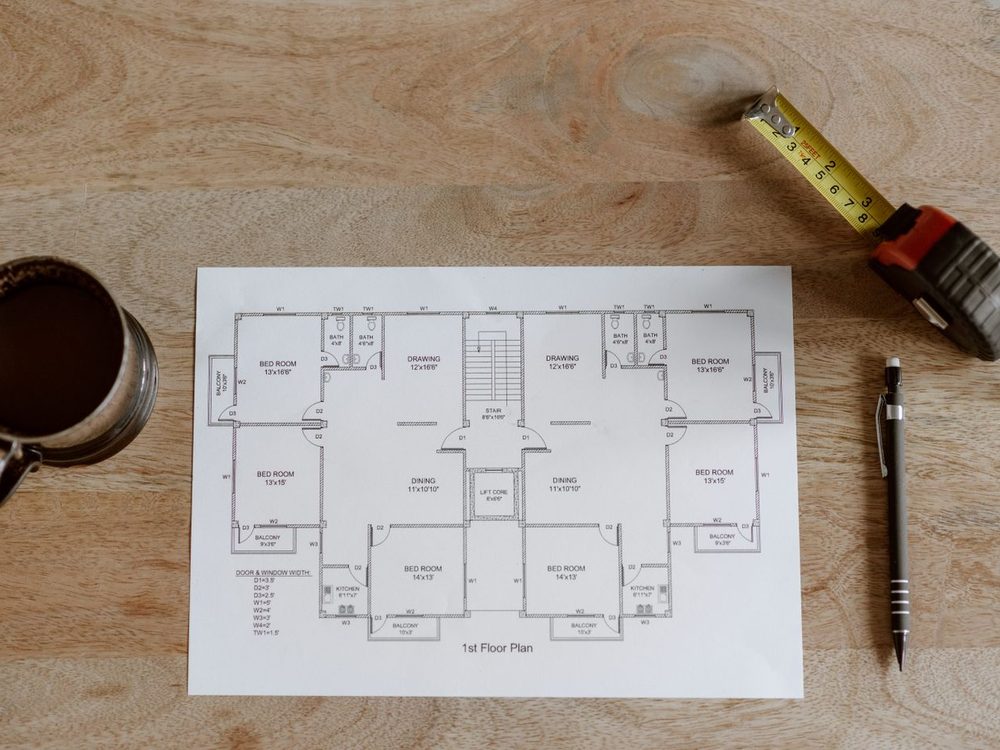 A house plan on a desk with a tape measure, pencil and scale rule laid across it