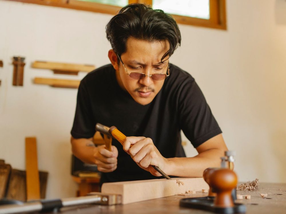 A carpenter cutting a notch in a hardwood plank with a chisel and mallet