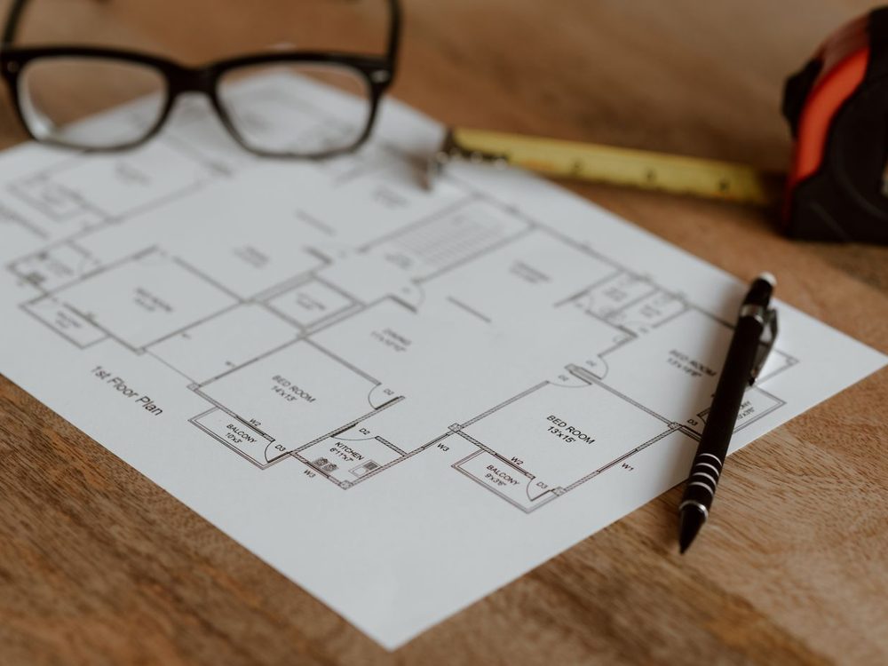 A house plan on a desk with a scale rule, pencil and reading glasses
